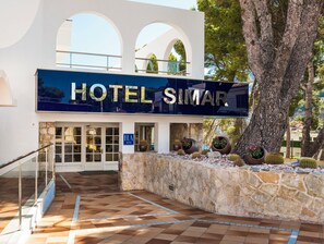 A hotel entrance with a stone wall, potted plants, and a clear sky. - Globales Simar (Pollença)