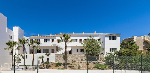 A modern multi-story building with balconies, surrounded by palm trees and a stone wall. - Globales Simar (Pollença)