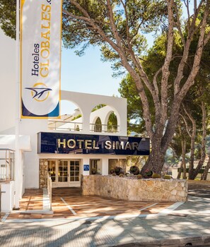 A hotel entrance with a stone facade, a large sign reading 'HOTEL SIMAR', and a flag with 'HOTEL GLOBALES' visible.