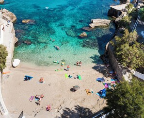 Una playa con agua cristalina, rocas y gente tomando el sol.