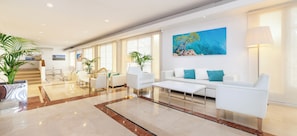 A spacious lobby with a marble floor, white sofas, a coffee table, and a painting on the wall.
