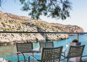 Una terraza con asientos al aire libre y vistas al mar y colinas rocosas.