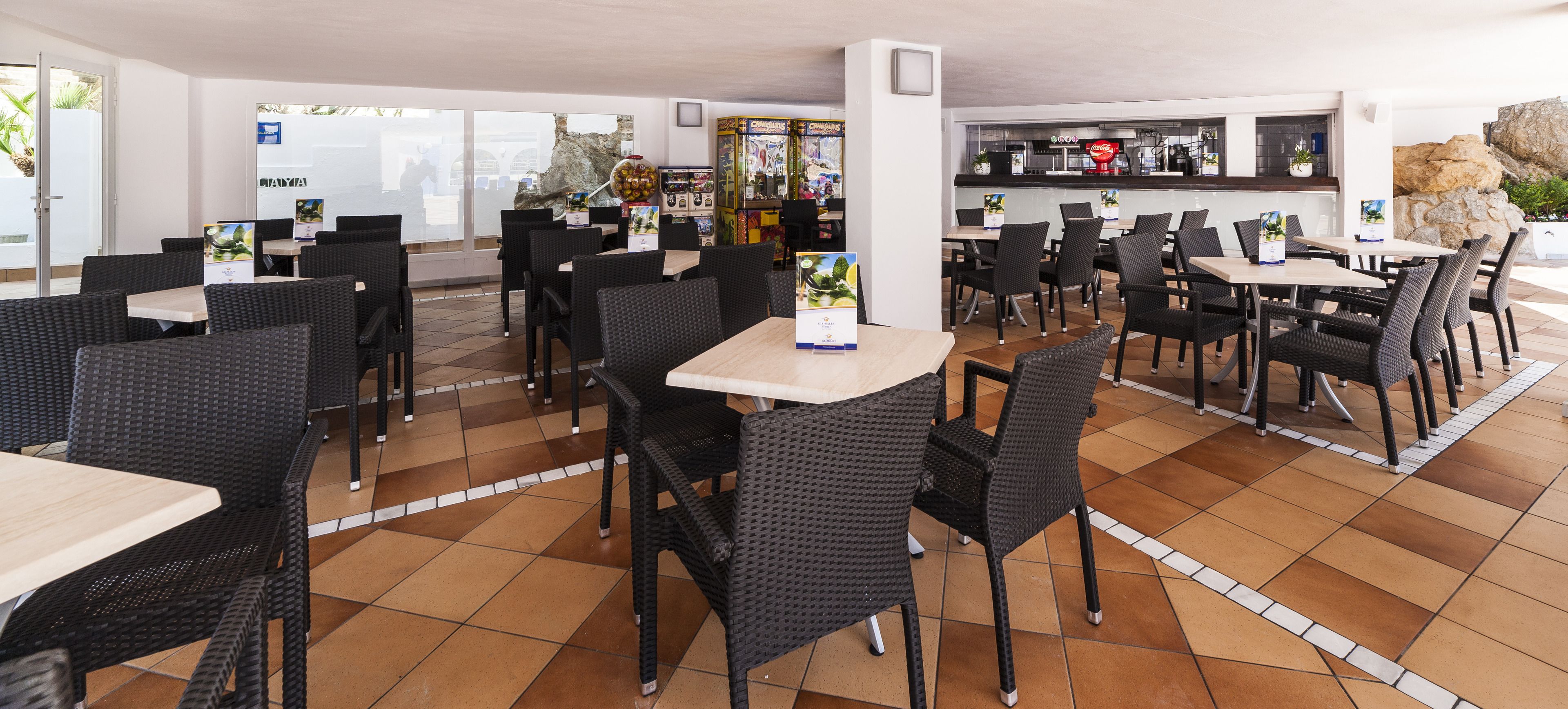 Un restaurante con mesas y sillas al aire libre, además de una zona de bar con mostrador y taburetes.