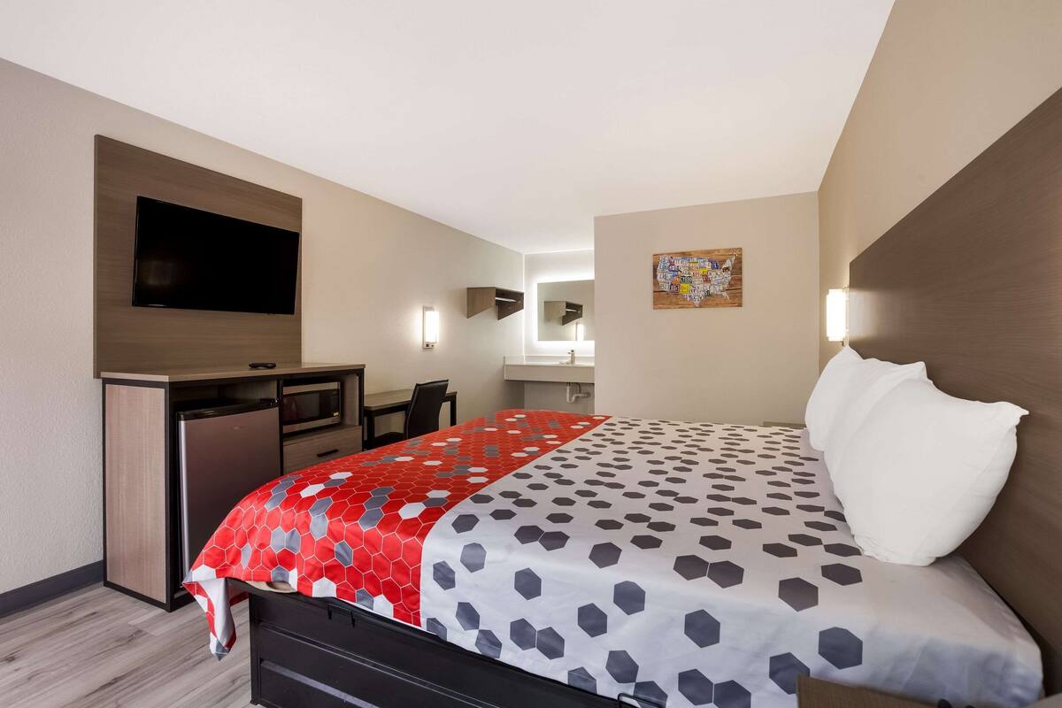 A hotel room with a bed, a desk, a television, and a bathroom visible in the background.