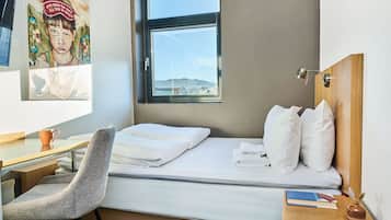 A hotel room with a bed, a desk, a chair, a window, and a painting on the wall.
