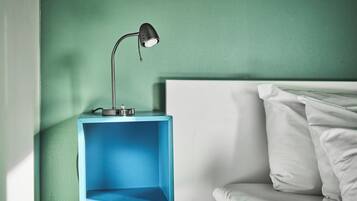 Una mesita de noche azul con una lámpara, una cama blanca y una pared verde.