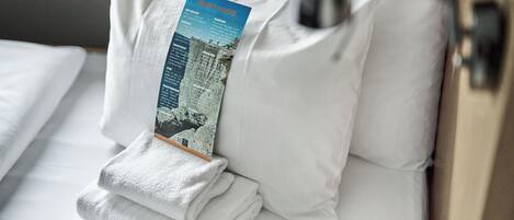 Un lit bien fait, avec des draps blancs, une serviette pliée et une brochure posée sur l’oreiller.