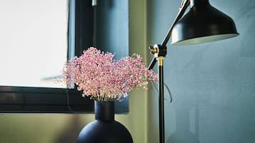 A vase with pink flowers on a windowsill next to a black desk lamp.