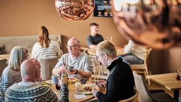 A group of people dining in a modern restaurant with a round table and a large, reflective spherical light fixture above.