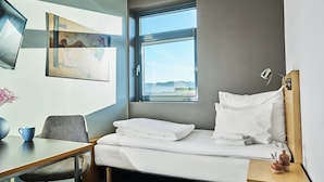 A hotel room with a bed, a desk, a chair, a window with a view, and a painting on the wall. - Smarthotel Forus (Sandnes)