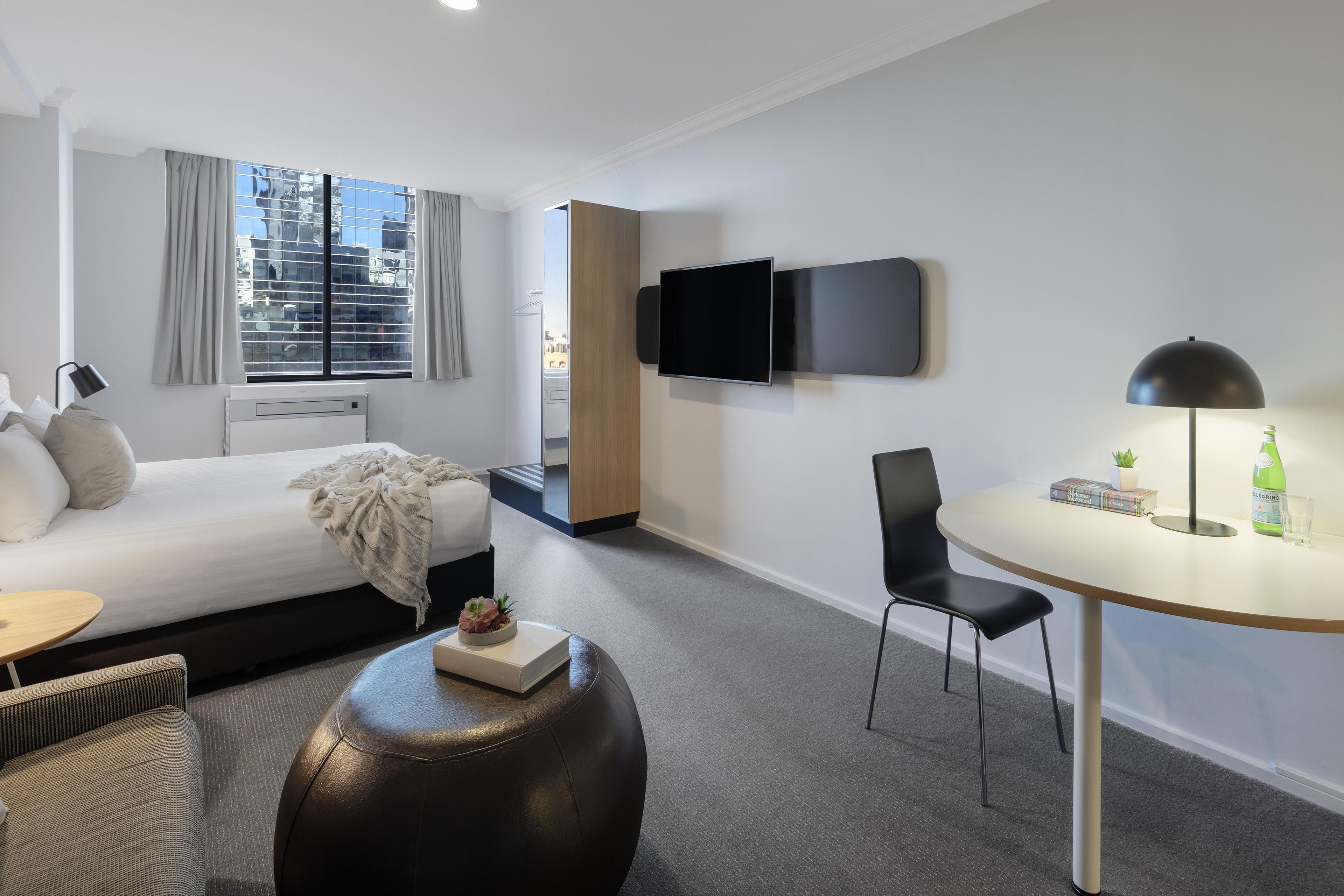 Una habitación de hotel moderna con cama, televisor de pantalla plana, una mesa de comedor redonda y un área de descanso con una silla.