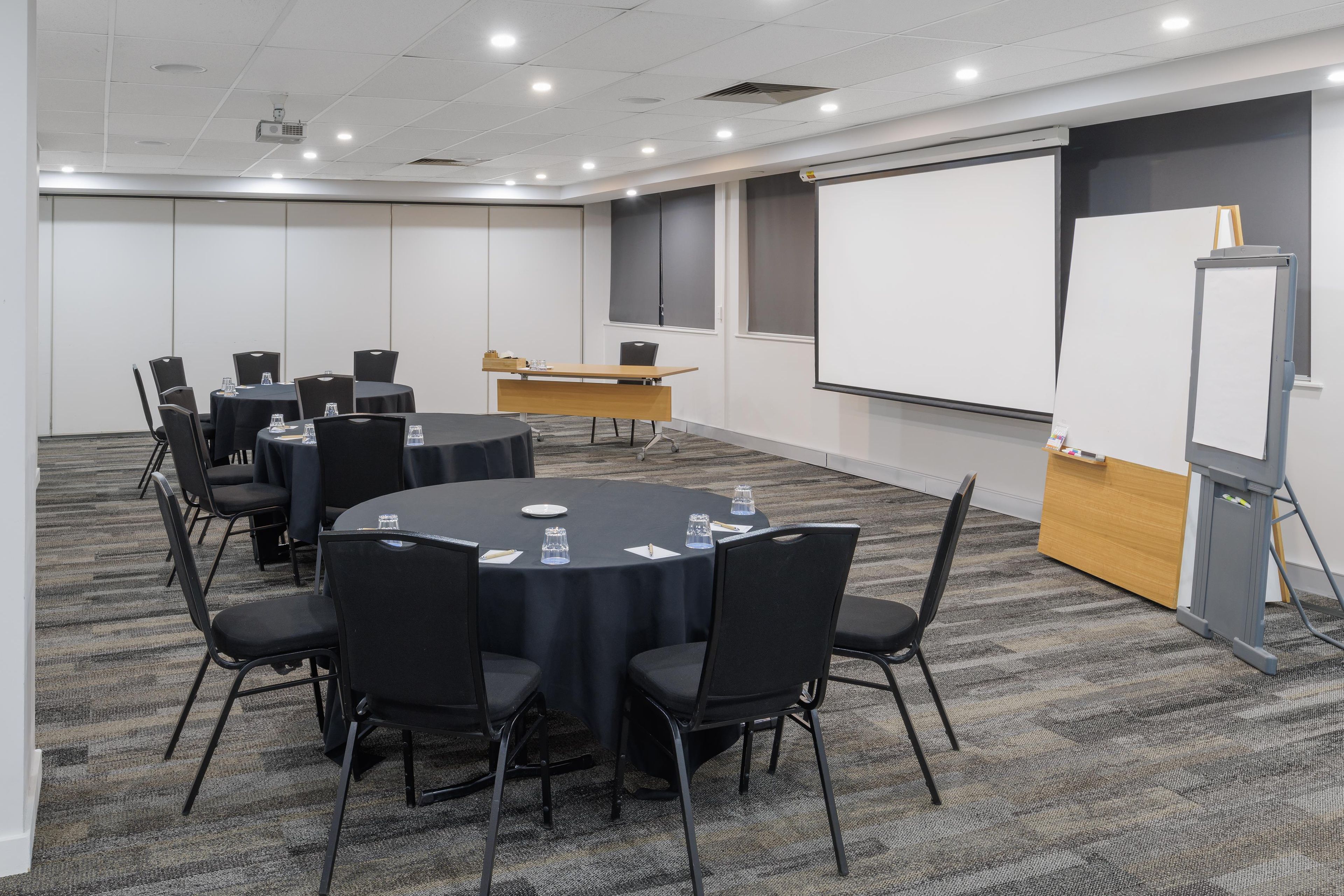 A conference room with a round table, black chairs, a whiteboard, and a projector.