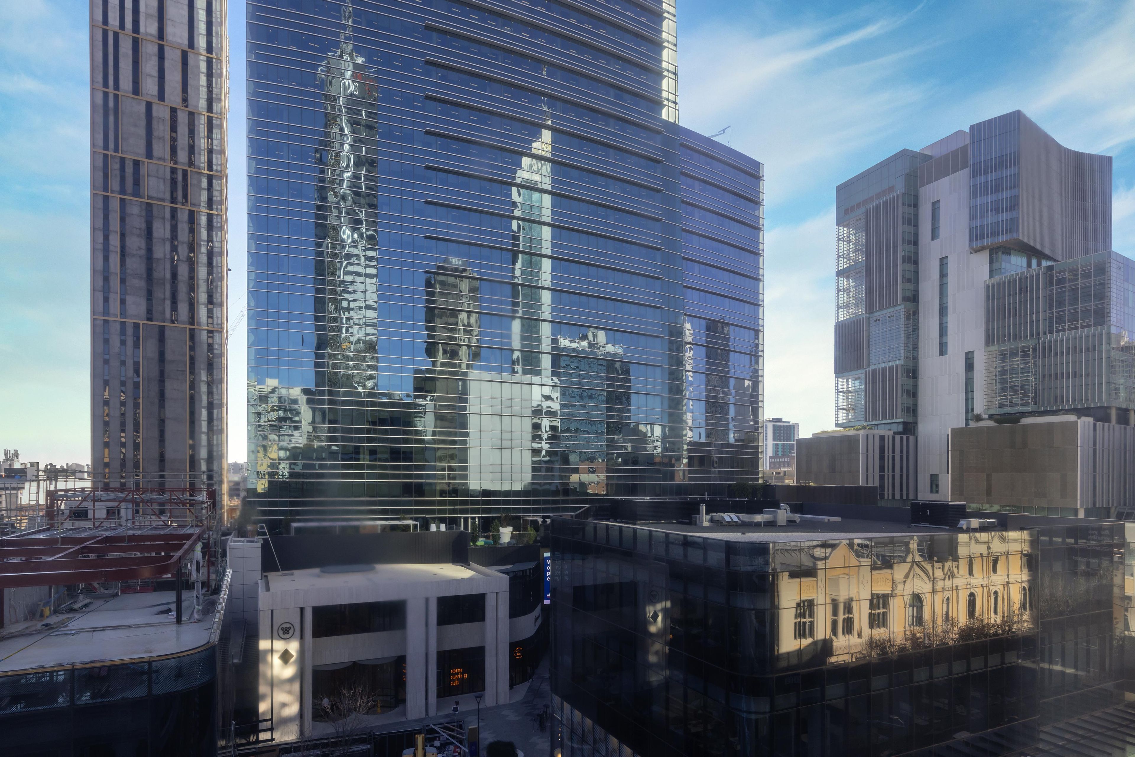 A modern high-rise building with a glass facade reflecting the surrounding cityscape.