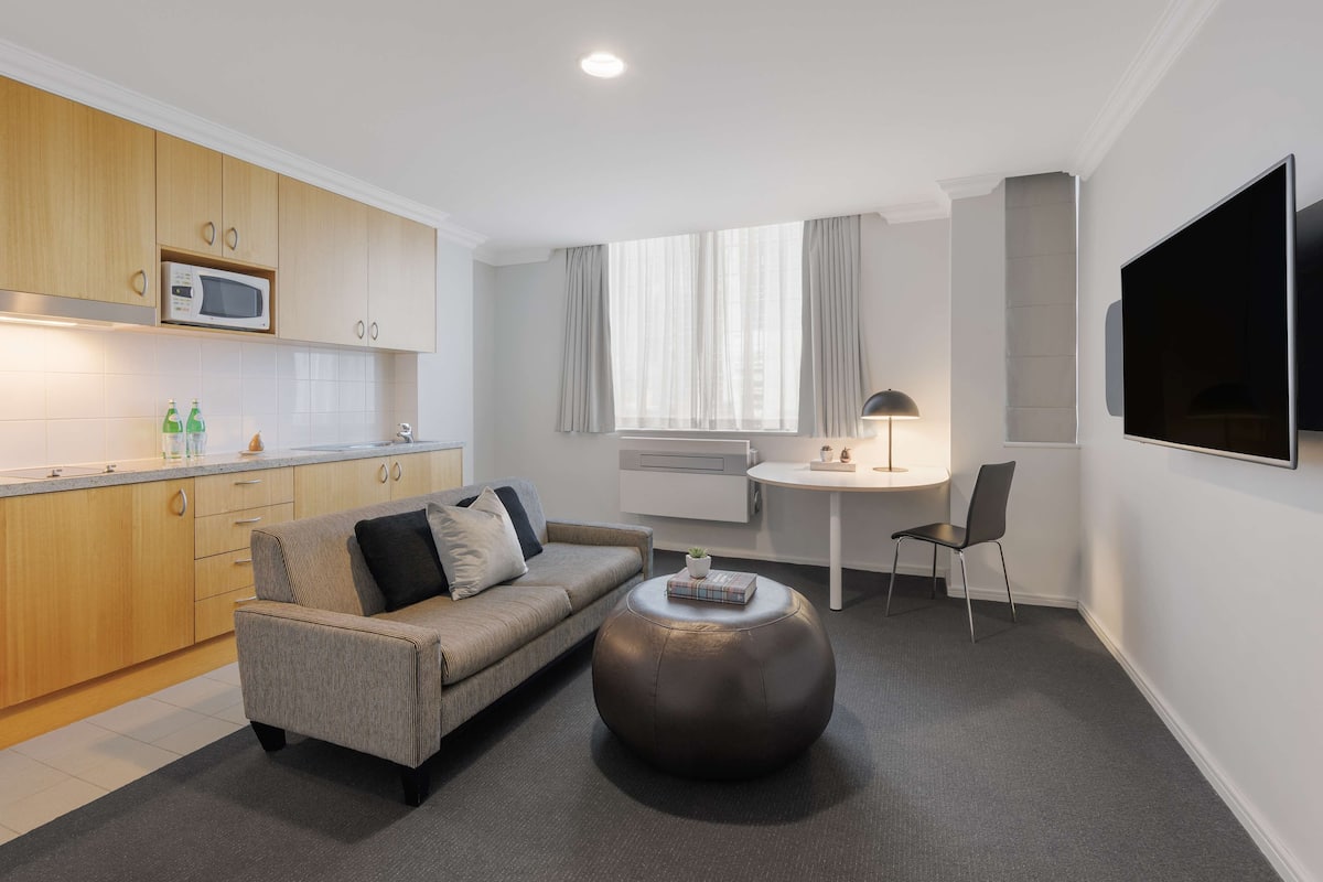 A modern living room with a sofa, ottoman, and a flat-screen TV mounted on the wall.