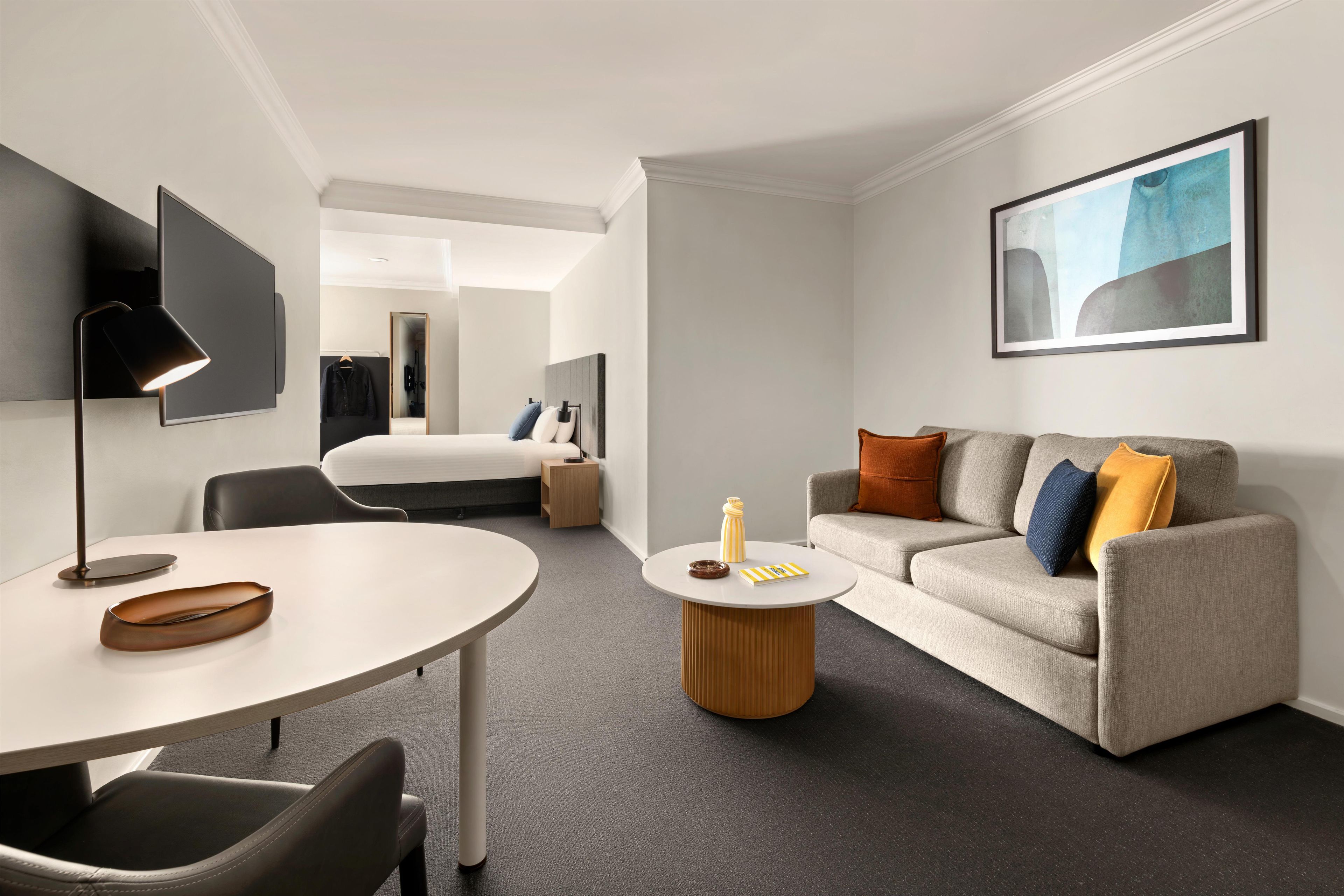 A modern hotel room with a bed, a sofa, a desk, and a TV.