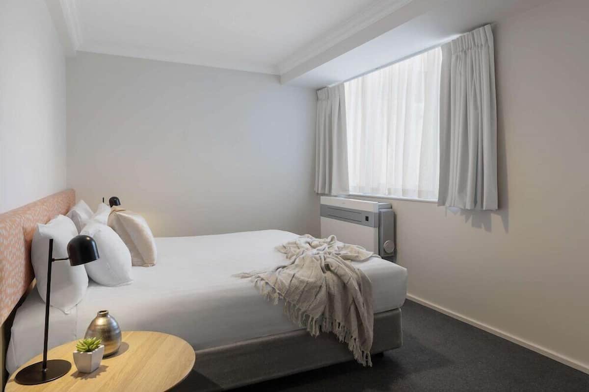 A bedroom with a bed, bedside lamp, and a small table with a plant.