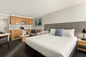 A hotel room with a large bed, a desk, a sofa, and a kitchenette. - Oaks Perth Hotel (Perth)