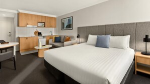 A hotel room with a large bed, a desk, a sofa, and a kitchenette. - Oaks Perth Hotel (Perth)