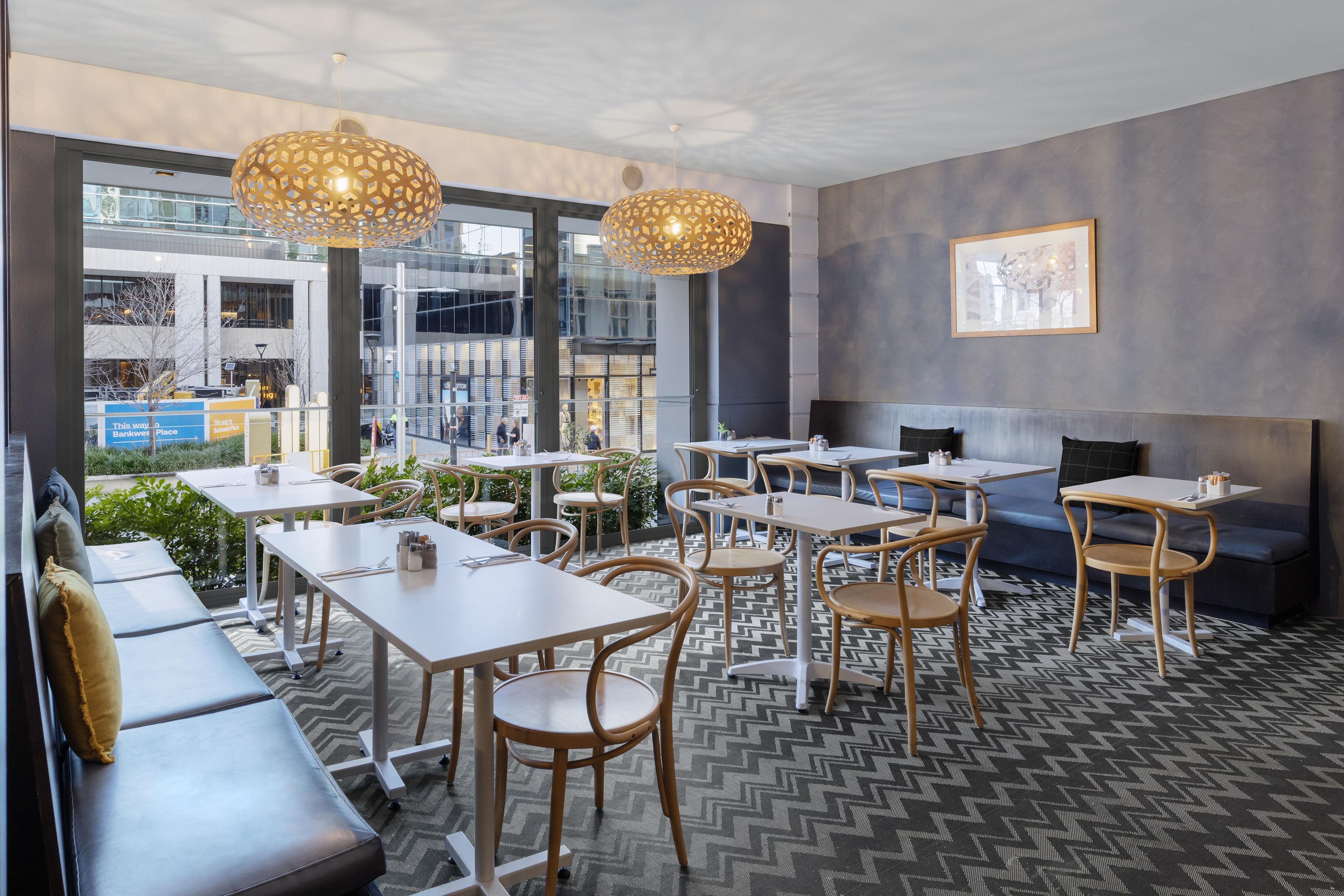 An indoor seating area with tables and chairs, large windows, and a patterned floor.
