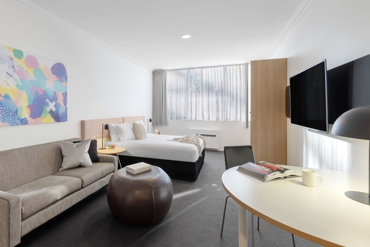 A modern hotel room with a sofa, a bed, a desk, and a TV.