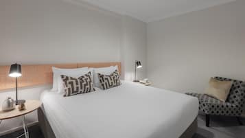 A hotel room with a large bed, two bedside tables, a nightstand, a lamp, a chair, and a coffee table.
