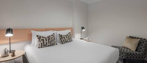 Une chambre d’hôtel avec un grand lit, deux tables de chevet, une commode, une lampe, une chaise et une table basse.