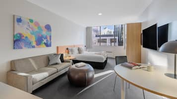 A modern hotel room with a sofa, a bed, a dining table, and a TV.