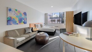 A modern hotel room with a bed, sofa, ottoman, and a dining area with a table and chairs. - Oaks Perth Hotel (Perth)