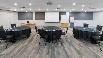 A conference room with four round tables, each with chairs, water glasses, and a projector.