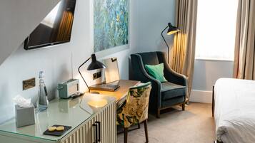 Une chambre d’hôtel avec un bureau en verre, une chaise, un lit, un téléviseur fixé au mur et une fenêtre avec des rideaux.
