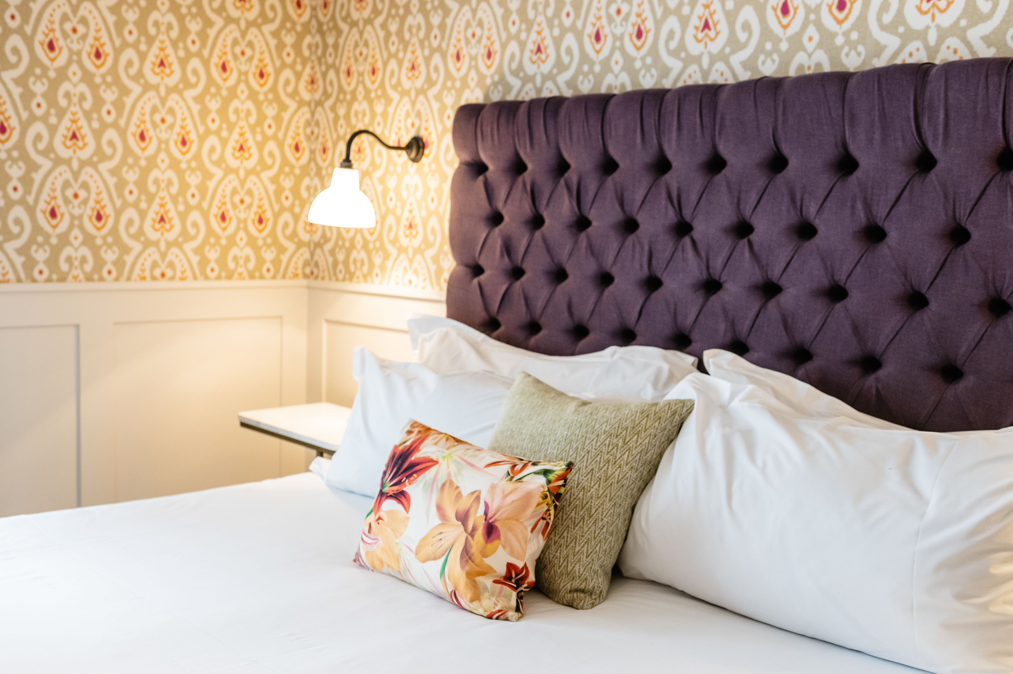 Un letto rifatto con cura, dotato di una testiera imbottita, biancheria bianca e cuscini decorativi.