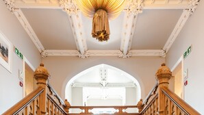 A grand staircase with ornate woodwork and a chandelier, leading to a bright hallway with a wooden floor. - Didsbury House Hotel (Manchester)