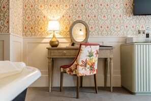 A hotel room with a wooden desk, a chair with a floral pattern, a round mirror, and a lamp. - Didsbury House Hotel (Manchester)