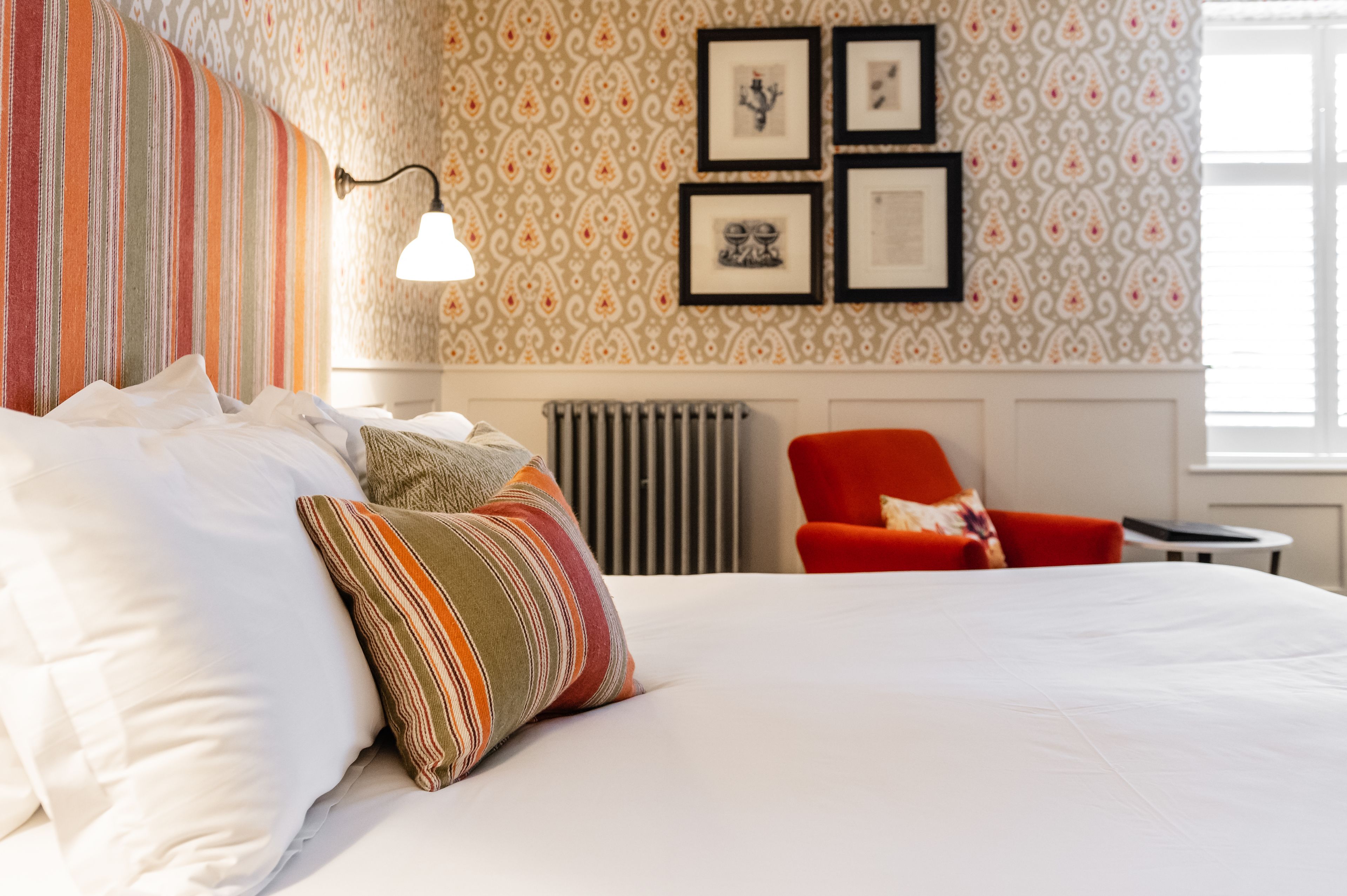 A hotel room with a large bed, striped pillows, a red armchair, and framed pictures on the wall.