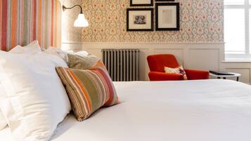 A hotel room with a large bed, striped pillows, a red armchair, and framed pictures on the wall.