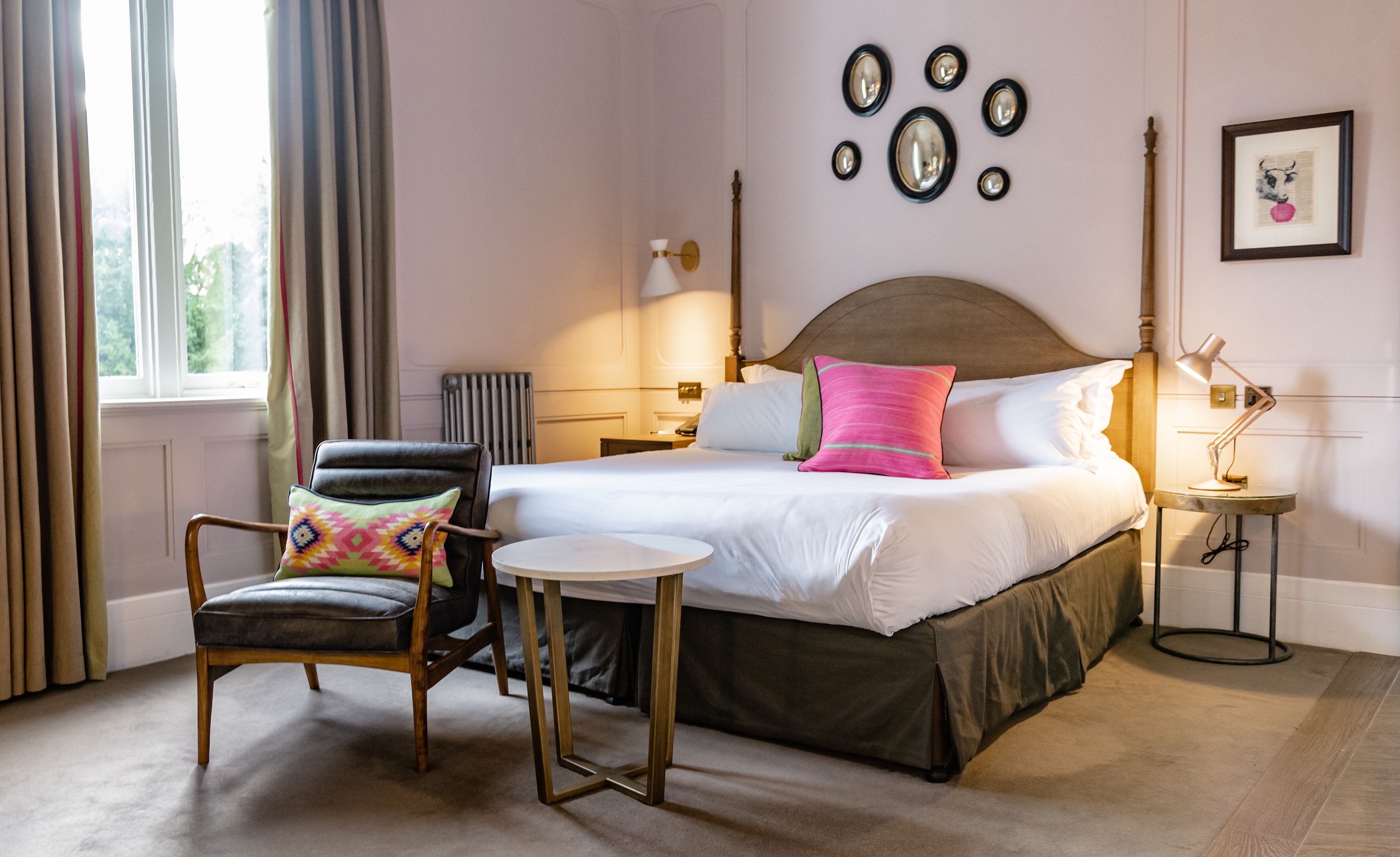 A hotel room with a bed, a chair, a small table, a lamp, and a picture on the wall.