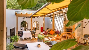 Un patio al aire libre con mobiliario de mimbre, una mesa con un florero y un toldo amarillo.