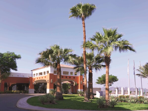 Traditional hotel with a central entrance, surrounded by palm trees and a well-manicured lawn.