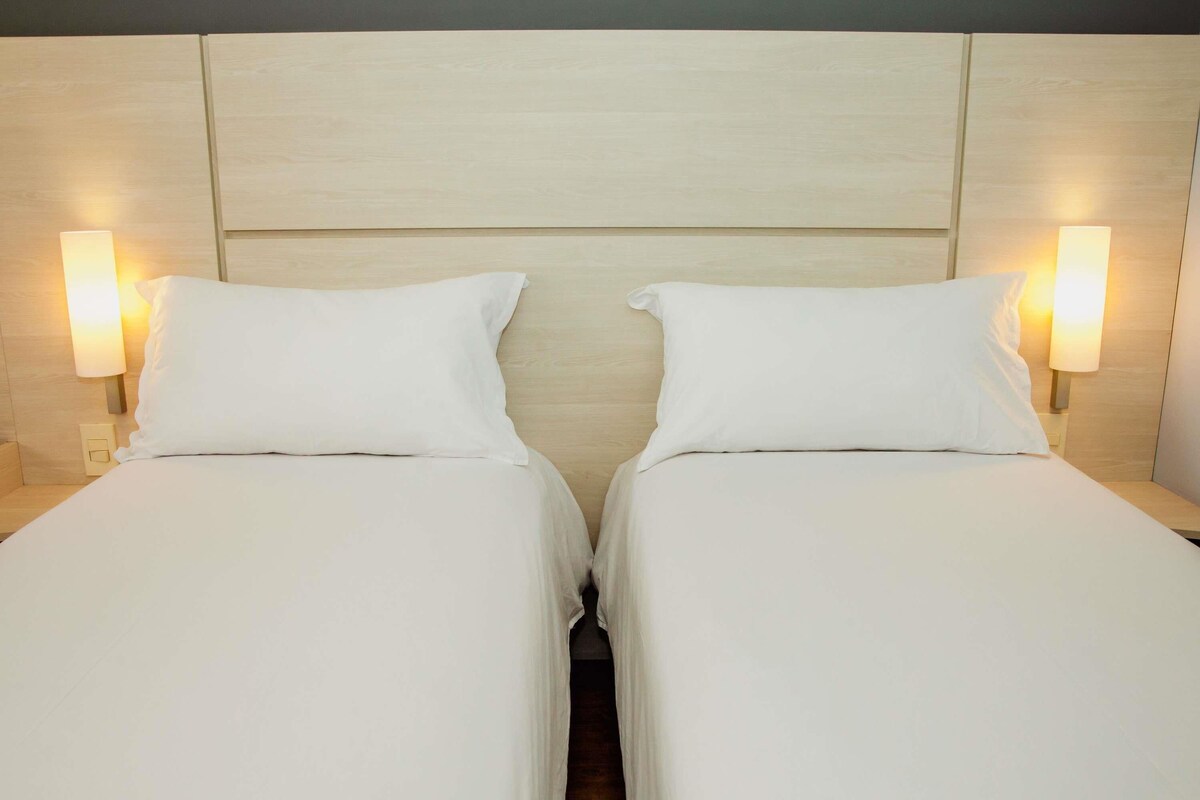 A double bed with a wooden headboard, two bedside lamps, and a neutral color scheme.