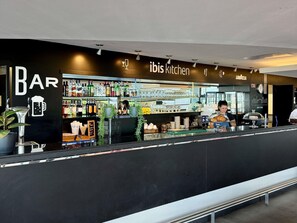Uma área de bar com balcão, prateleiras cheias de garrafas e uma placa que diz 'ibis kitchen'.