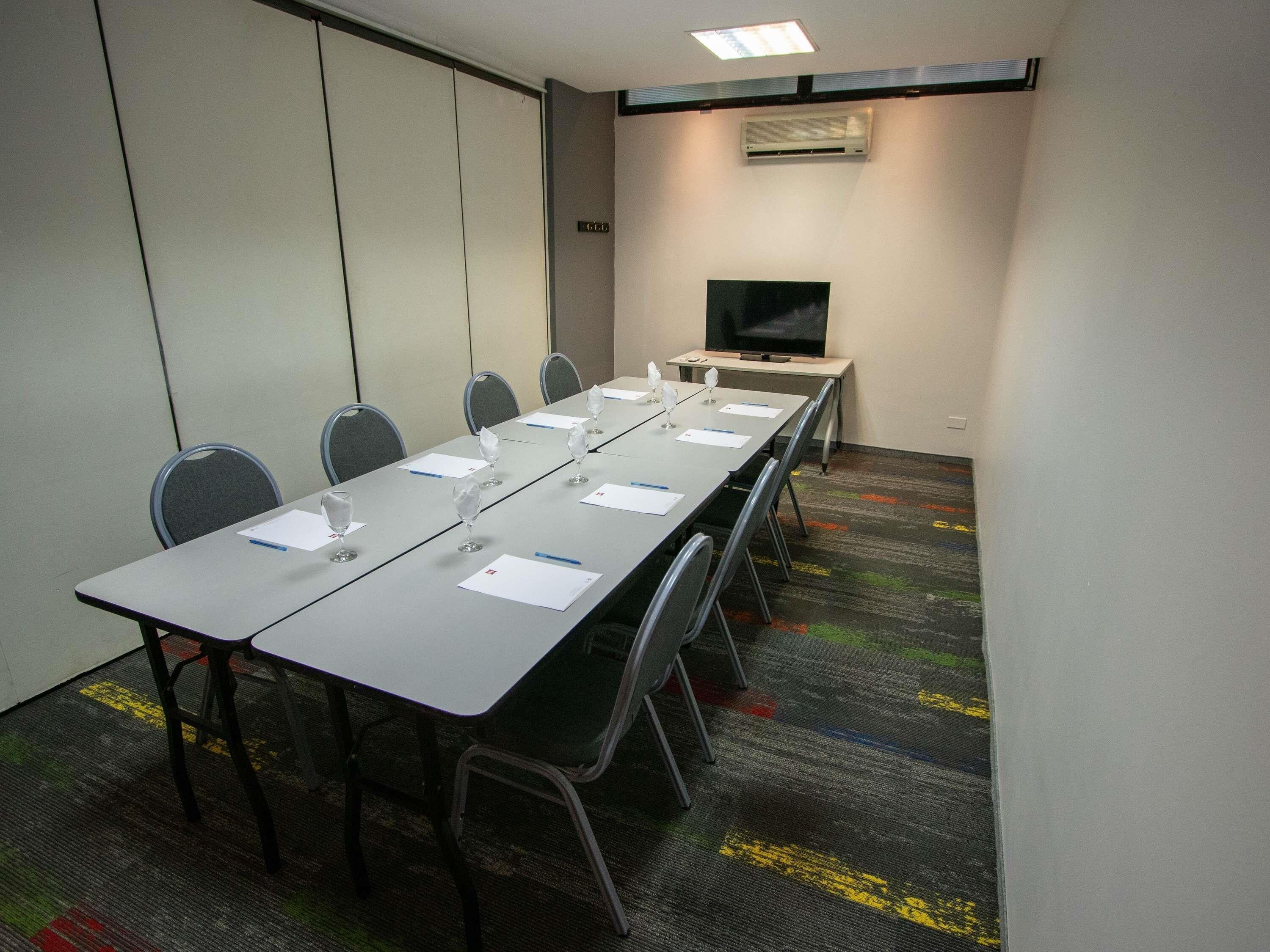Une salle de conférence équipée d’une longue table, de chaises, d’un téléviseur et d’un appareil de climatisation.