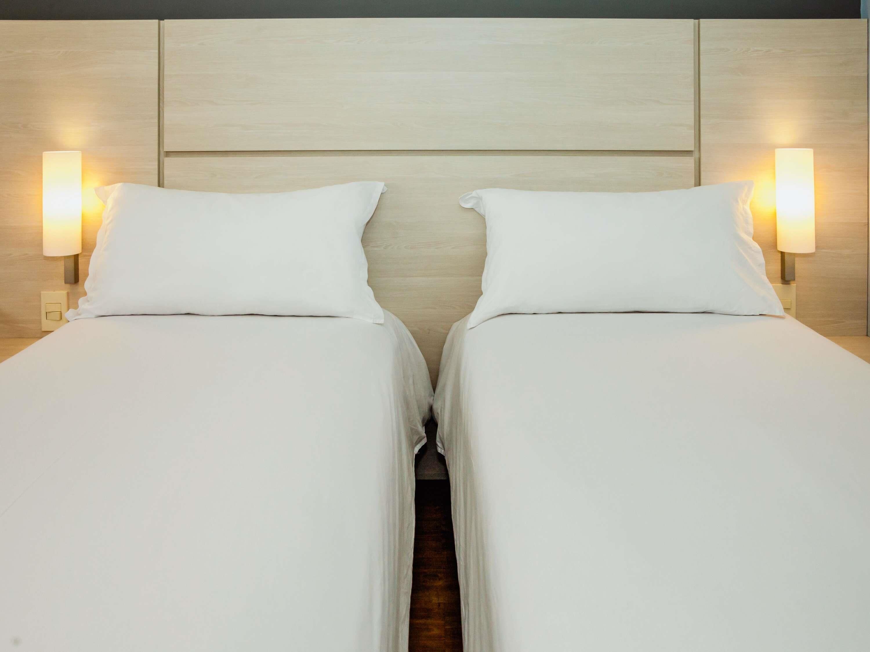 A double bed with white linens and two bedside lamps.