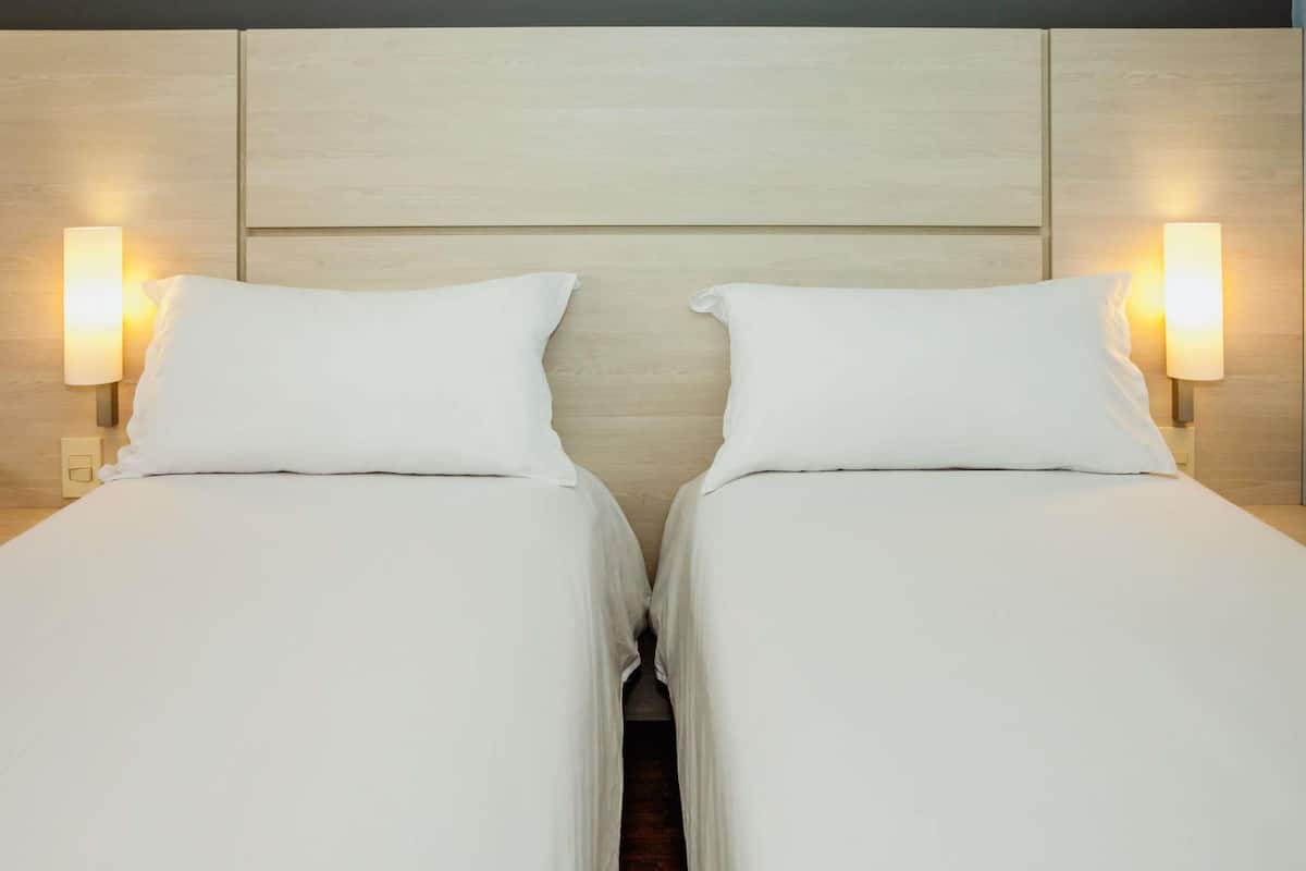 A double bed with white linens and two bedside lamps.