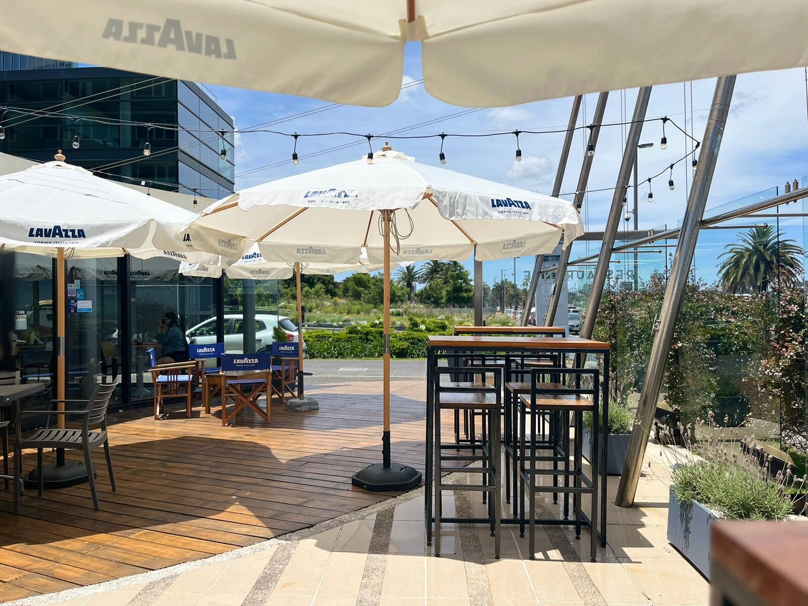 Zona d'aigüda exterior amb ombrel·les blanques amb la marca "LAVAZZA", taules de fusta i cadires.