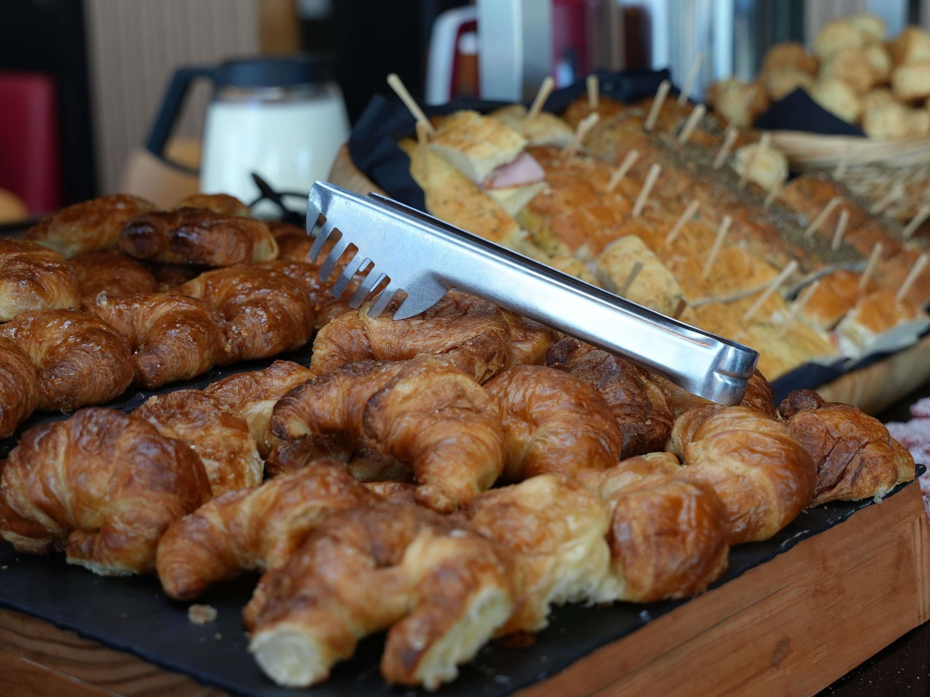 Una bandeja con varios pasteles, incluyendo croissants y palitos de pan, con un utensilio para servir encima.