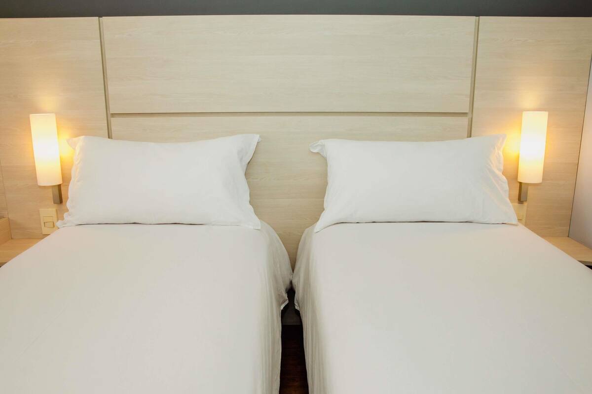 A double bed with a wooden headboard, two bedside lamps, and a neutral color scheme.