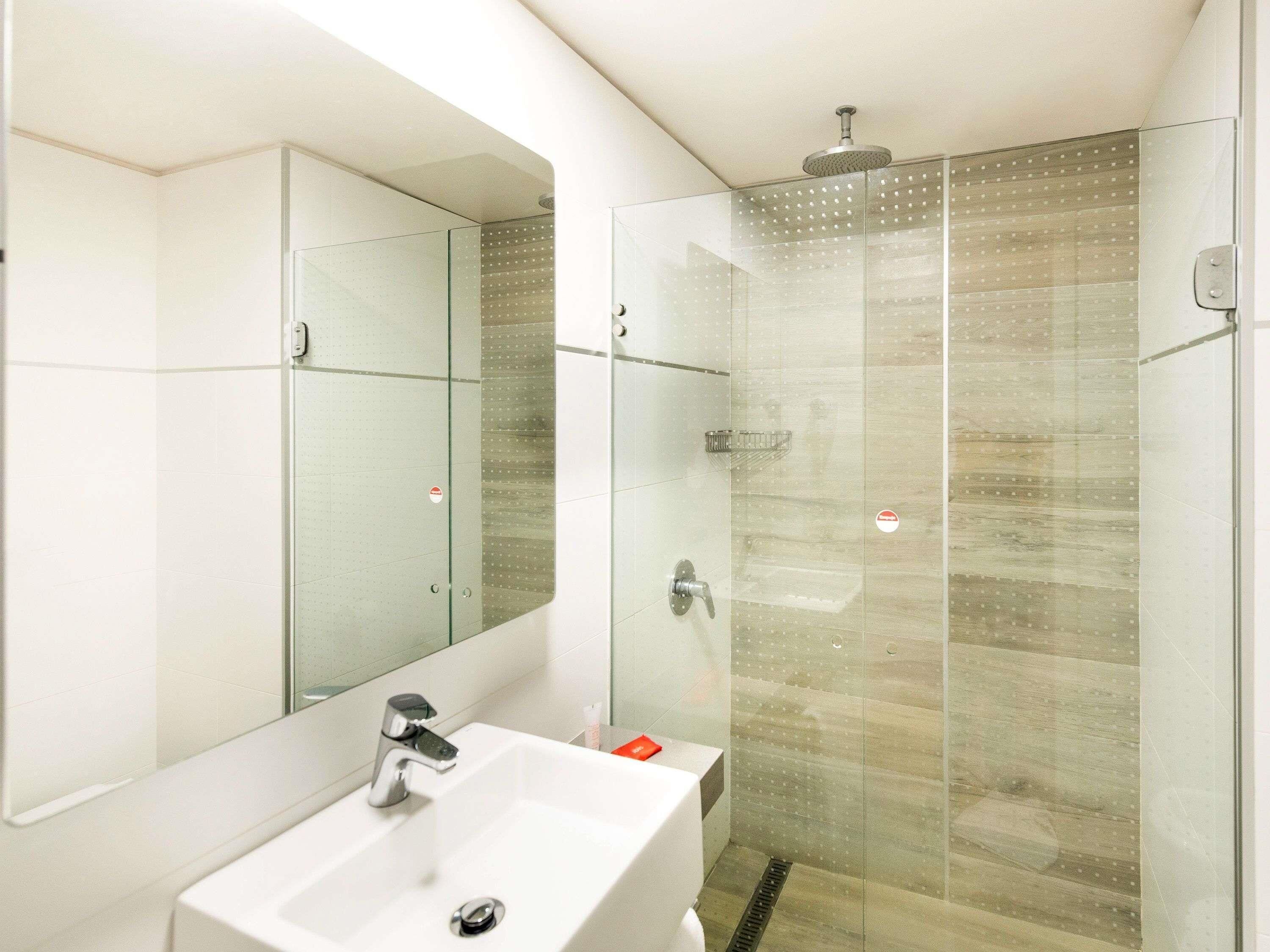 Un baño moderno con ducha de vidrio, lavamanos blanco y un espejo grande.