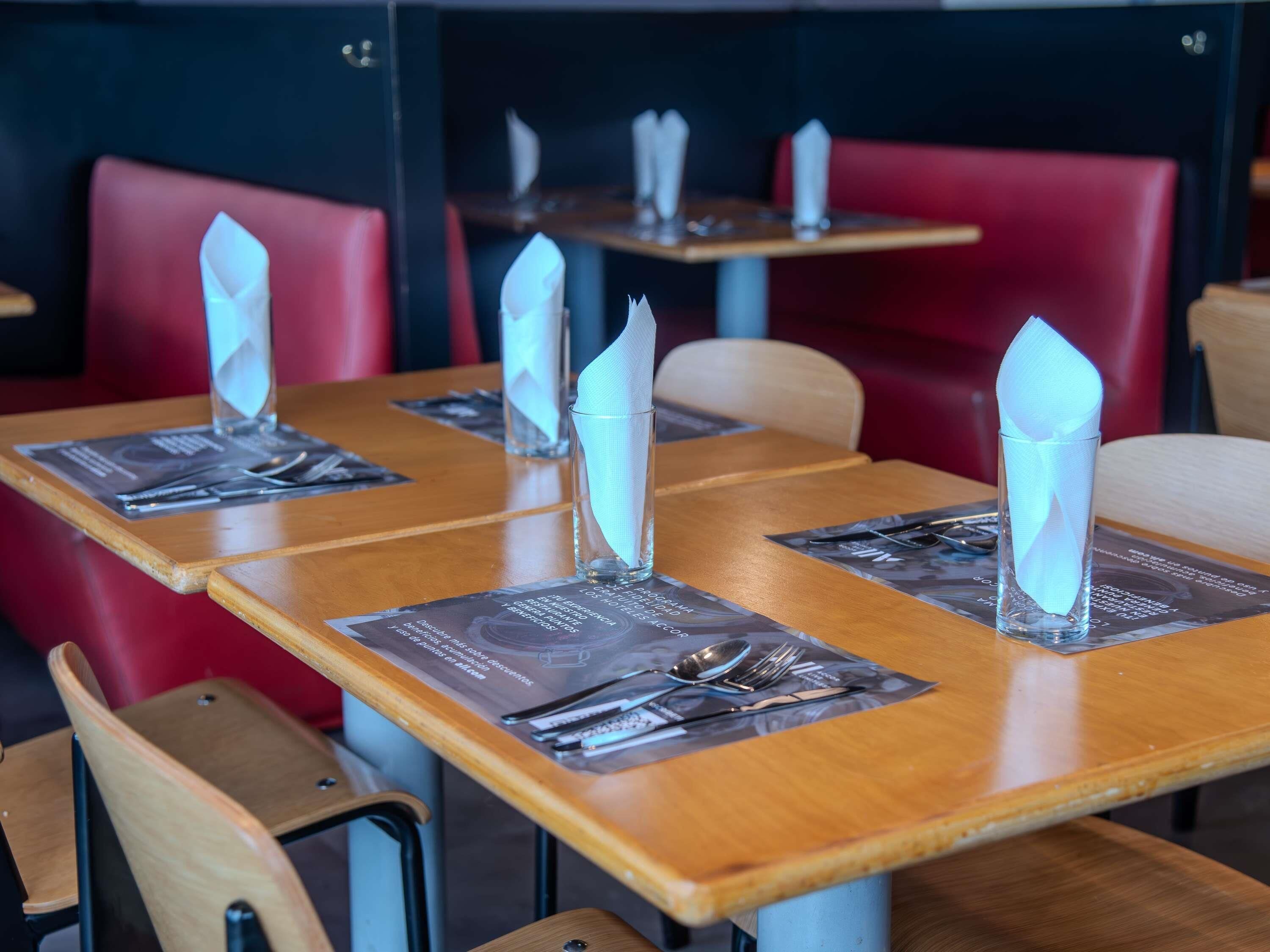 A restaurant interior with wooden tables, red upholstered chairs, and clear plastic napkins on place settings.
