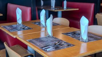 A restaurant interior with wooden tables, red upholstered chairs, and clear plastic napkins on place settings.