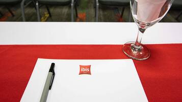 Una mesa con mantel rojo, un bolígrafo, un vaso con servilleta y un papel con el logotipo de 'ibis Hotels'.